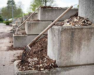Reihen von großen Betonbehältern mit Mulch und aufgestützten Gartenhacken im Freien